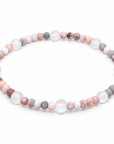 A beaded stretch bracelet made of round gemstone beads in soft pink, white, gray, and peach tones, arranged in a circle on a plain white background.