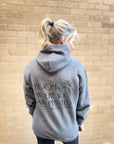 Person wearing a gray hoodie with text on the back against a brick wall