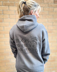 Person wearing a gray hoodie with text and floral design against a brick wall