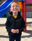 Child wearing a black hoodie with text on a playground