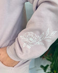 Close-up of a light pink sweatshirt with a floral design on the sleeve.