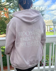 Person wearing a hoodie with 'Bloom Where You Are Planted' text on a balcony.