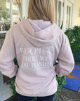 Person wearing a light pink hoodie with text on the back, standing outdoors.