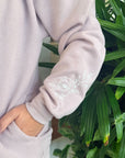 Light gray sweatshirt with white floral embroidery against a green plant background