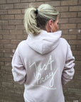 Person wearing a light gray hoodie with 'Just Pray' text on the back, standing against a brick wall.