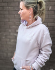 Woman wearing a light gray hoodie with text, standing against a brick wall.