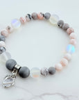 Beaded bracelet with gray, pink, and white beads and a heart charm on a marble surface.