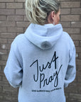 Person wearing a gray hoodie with 'Just Pray' text on the back against a brick wall.