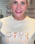 Woman wearing a light-colored sweatshirt with 'He is Risen' text and lamb graphic.