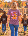 A woman and two children walk away in a pumpkin patch wearing matching brown hoodies with white 'Just Pray' text on the back. The woman's tee features a large colorful autumn graphic with pumpkins, flowers, and the phrase 'Jesus is the reason for the season.
