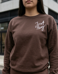 Person wearing a brown sweatshirt with 'Just Pray' text in white, standing in an urban setting.