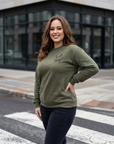 Woman wearing a green sweatshirt with text on it, standing on a street corner.