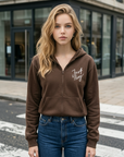 Woman wearing a brown hoodie with text on it, standing on a street.