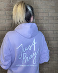Person wearing a lavender hoodie with 'Just Pray' text on a tiled floor.