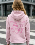 Person wearing a pink hoodie with text on the back, standing on a street.