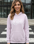 Woman wearing a light purple hoodie with 'Praise the Lord' text, standing on a street.