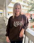 Woman wearing a brown sweatshirt with 'PRAISE THE LORD' text on a porch.