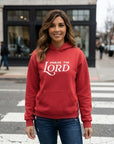 Woman wearing a red hoodie with 'Praise the Lord' text on a city street.