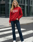 Person wearing a red hoodie with text standing on a crosswalk.