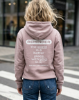 Person wearing a pink hoodie with a motivational quote on the back, standing on a crosswalk.