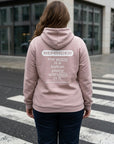 Person wearing a pink hoodie with a motivational message on the back, standing on a street.