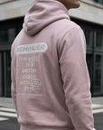 Person wearing a pink hoodie with a motivational message on the back, standing in an urban setting.