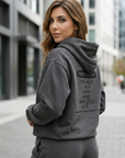 Woman wearing a gray hoodie with text on the back in an urban setting