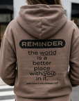Person wearing a brown hoodie with a motivational message on the back, standing on a crosswalk.