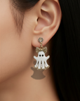 A close-up of a model's ear wearing a dangling earring with a white ghost charm, gold-tone bow details, and small clear rhinestones.