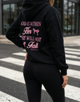 Person wearing a black hoodie with pink text on the back, standing on a crosswalk.