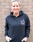 Woman wearing a black hoodie with 'Just Pray' text against a brick wall.