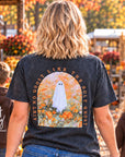 A woman and two children walk down a fall-themed pumpkin patch aisle, viewed from behind. The woman wears a dark charcoal graphic T-shirt with a ghost illustration and the words 'Ain't no ghost like the holy Ghosts,' while the children wear matching brown hoodies with 'Just Pray' written on the back.