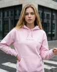 Woman wearing a pink hoodie with text, standing on a street.