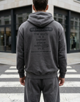 Person wearing a gray hoodie with a motivational message on the back, standing on a city street.