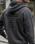 Person wearing a gray hoodie with a motivational message on the back, standing in an urban setting.