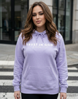 Woman wearing a lavender hoodie with text, standing on a crosswalk.
