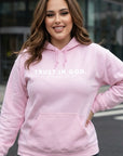 Person wearing a pink hoodie with 'TRUST IN GOD' text outdoors.