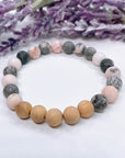 A Pink Zebra Jasper and Cedar Wood gemstone stretch bracelet sits on a white table.