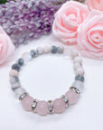 A Rose Quartz Rhinestone Companion Gemstone stretch bracelet made with 4 pink rose quartz gemstones, translucent aura beads, pink jasper gemstones, and rhinestone accents for added sparkle sits on a white table.