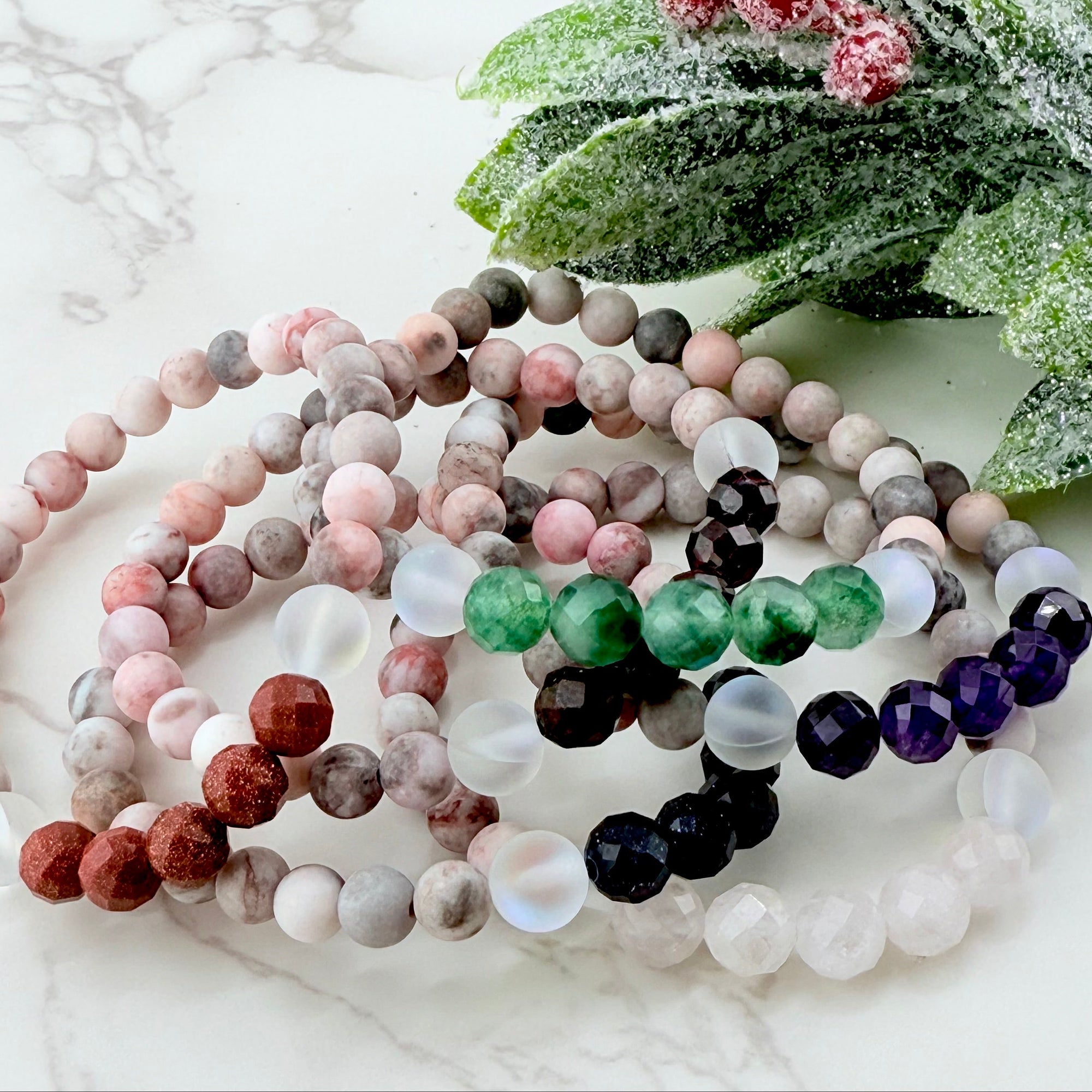 Set of beaded bracelets on a white surface with greenery in the background
