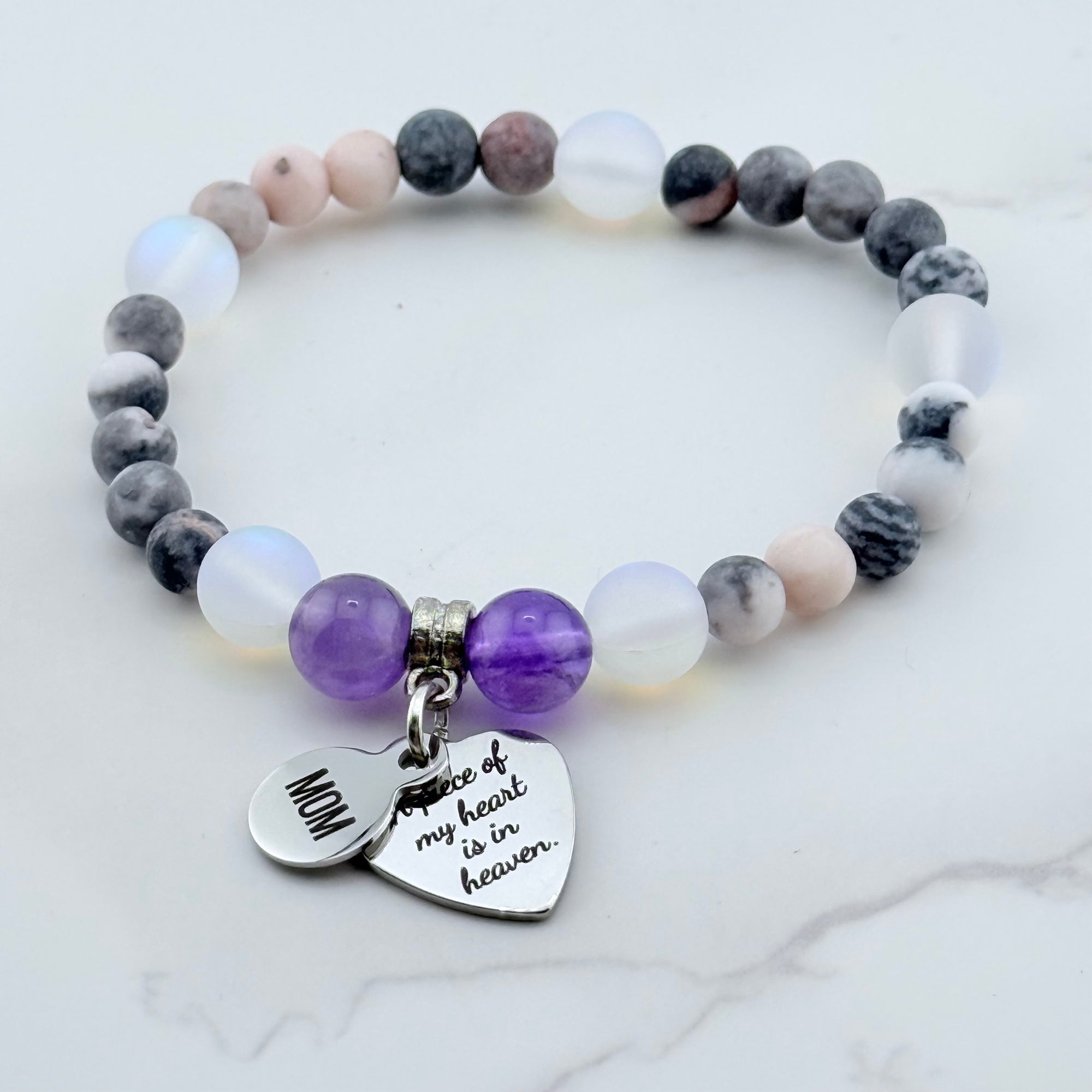 Beaded bracelet with heart-shaped charm and engraved text on a marble background