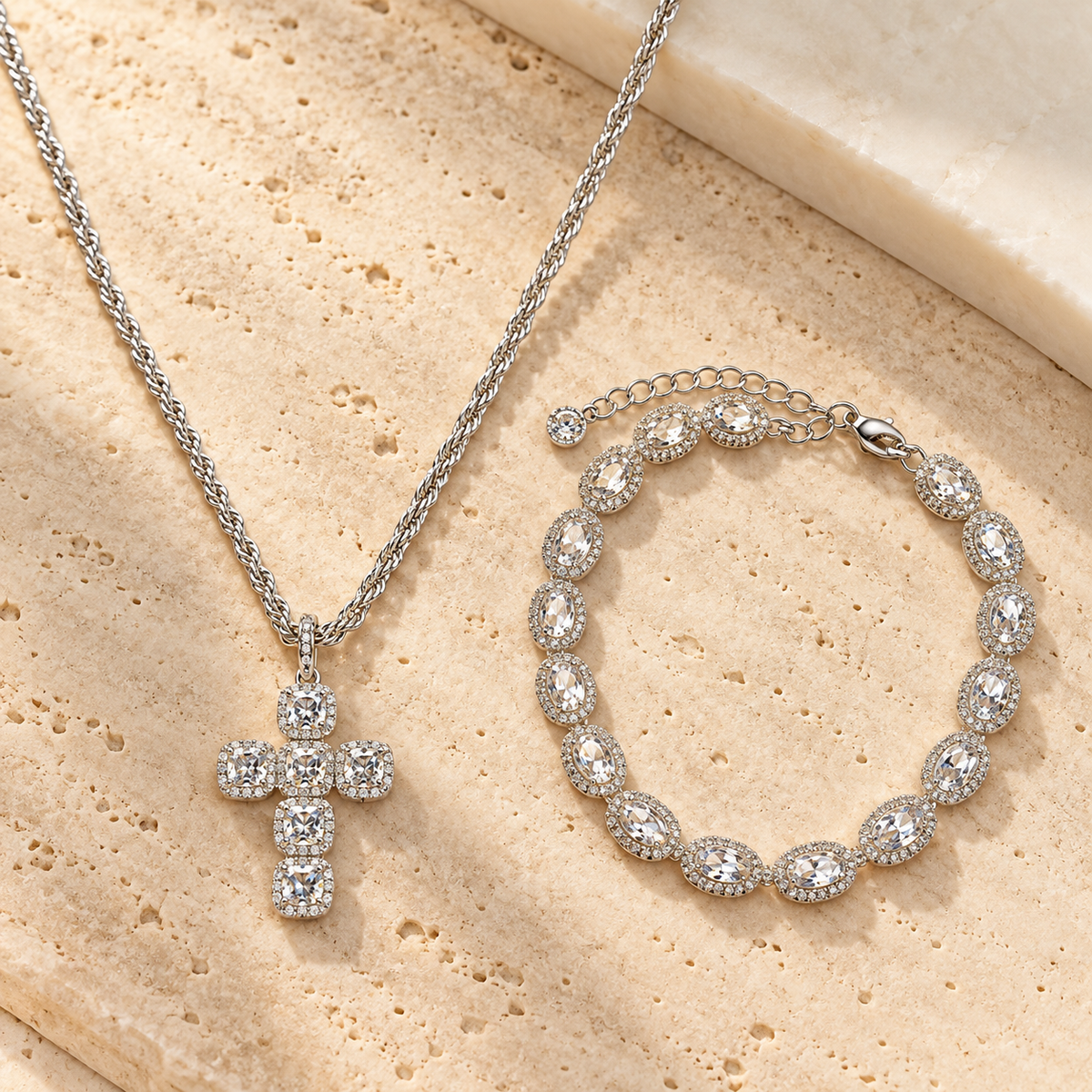 Silver cross pendant necklace and matching beaded bracelet with clear stones, displayed on a beige stone surface.