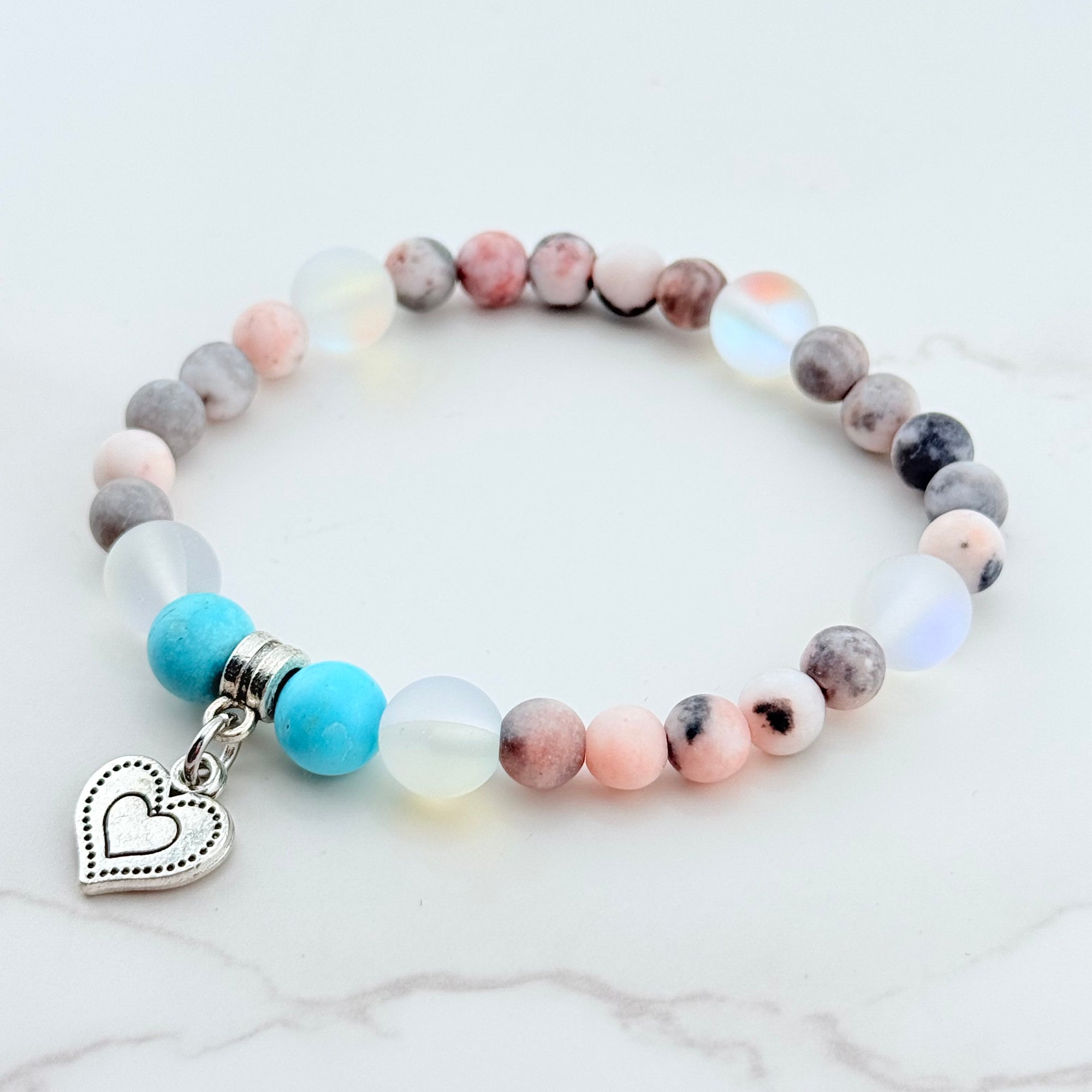 Multicolored beaded bracelet with a heart charm on a white marble surface