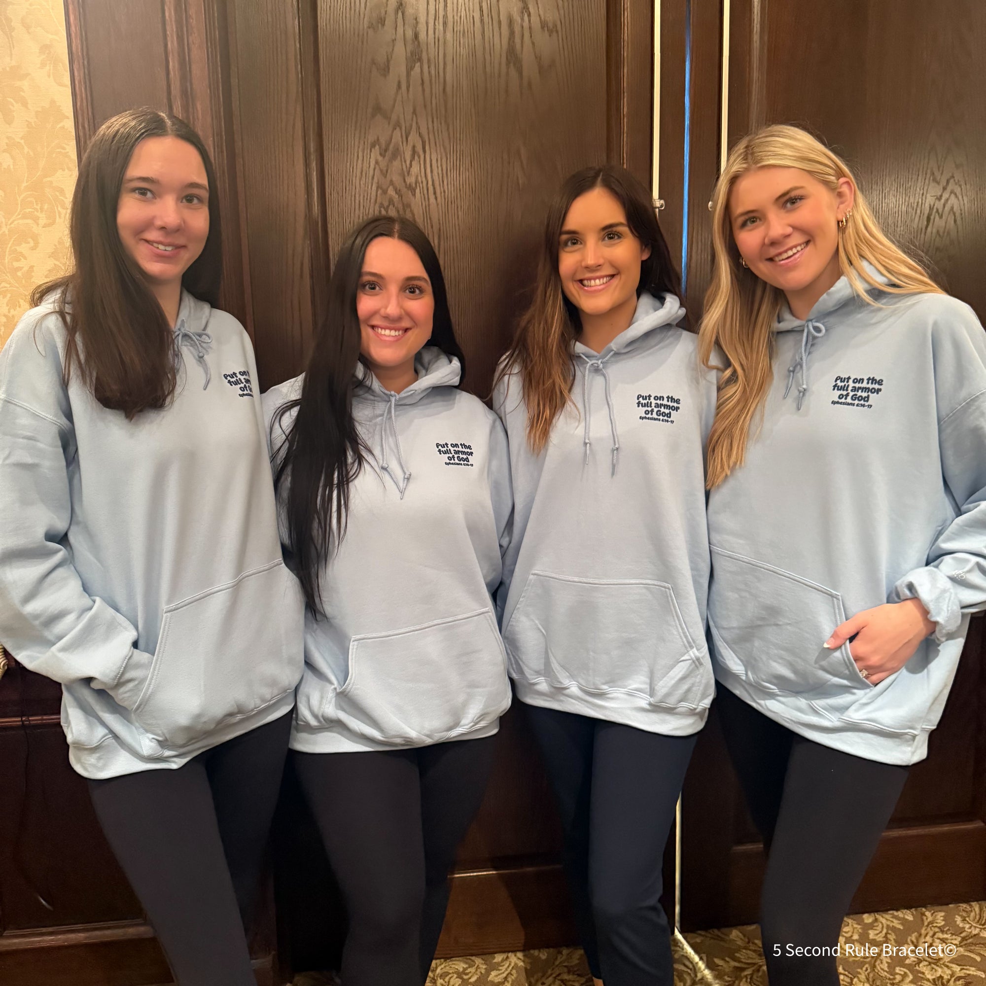 Four women wearing matching gray hoodies in a hallway.