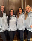 Four women wearing matching gray hoodies in a hallway.