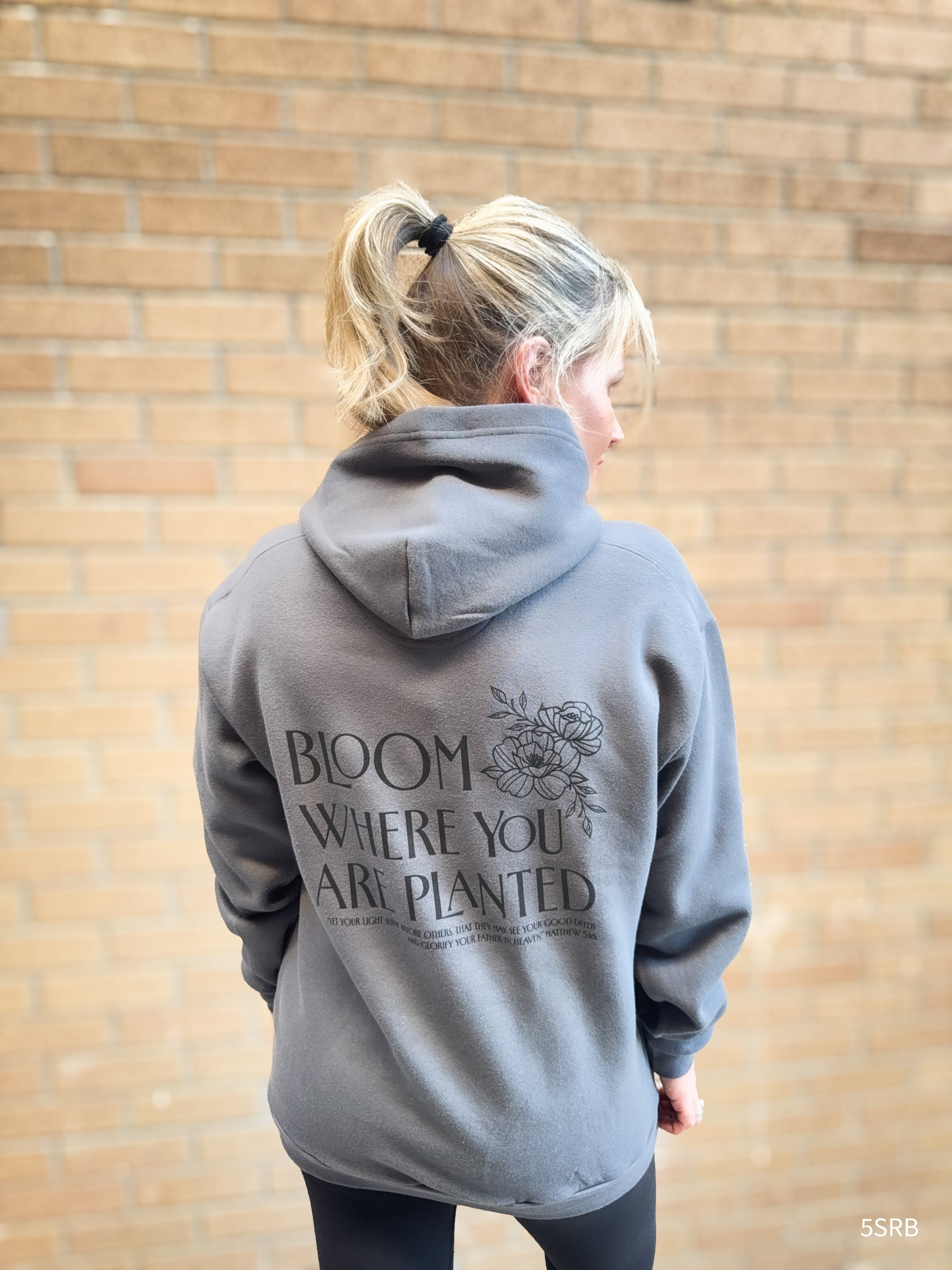 Person wearing a gray hoodie with text on the back against a brick wall