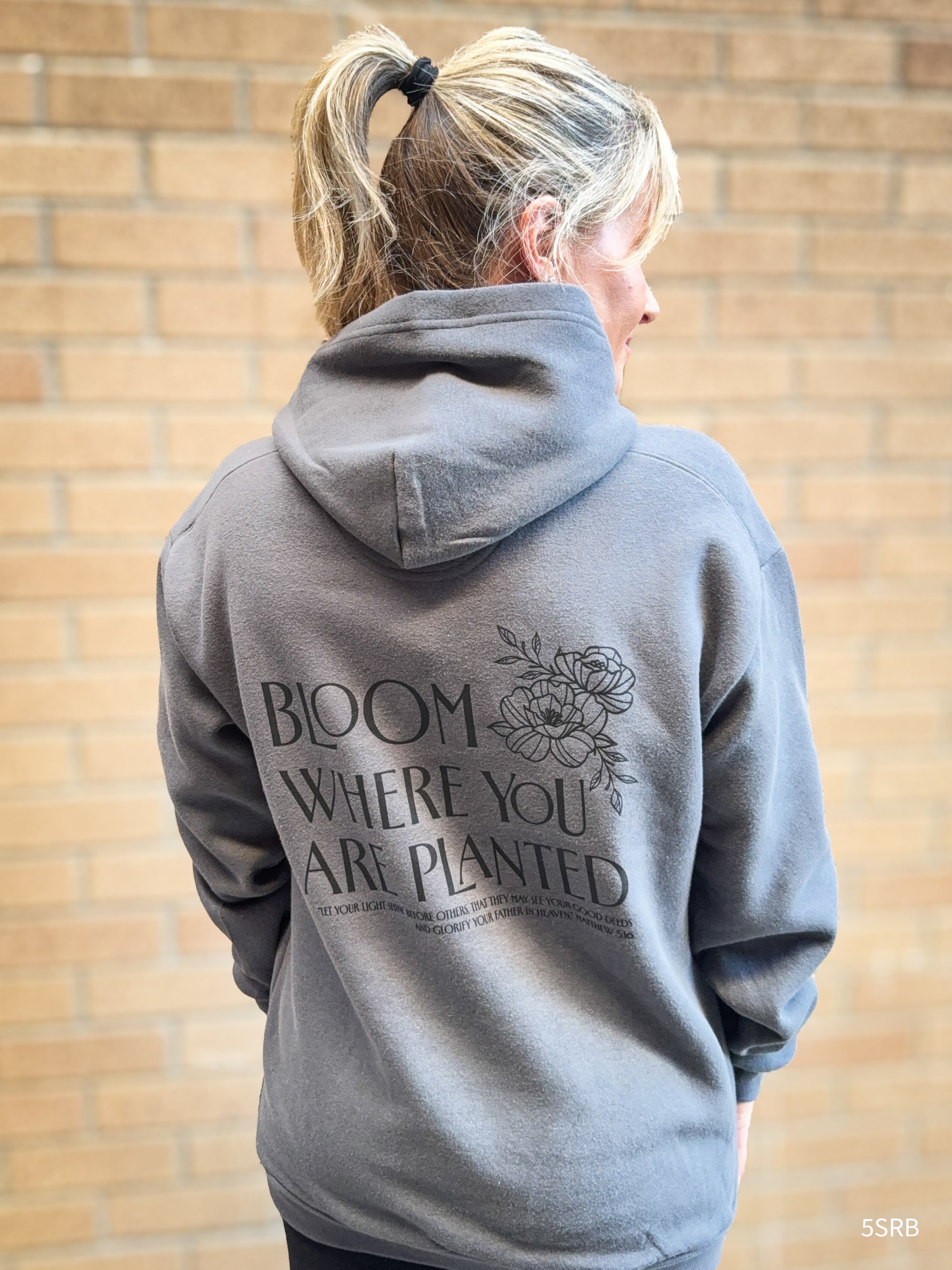 Person wearing a gray hoodie with text and floral design against a brick wall