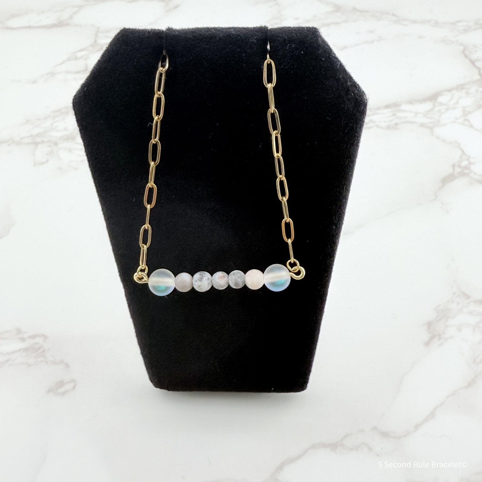 Necklace with gold chain and round beads on a black stand against a marble background