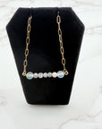 Necklace with gold chain and round beads on a black stand against a marble background