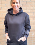 Woman wearing a dark gray hoodie with a floral design on a brick wall background